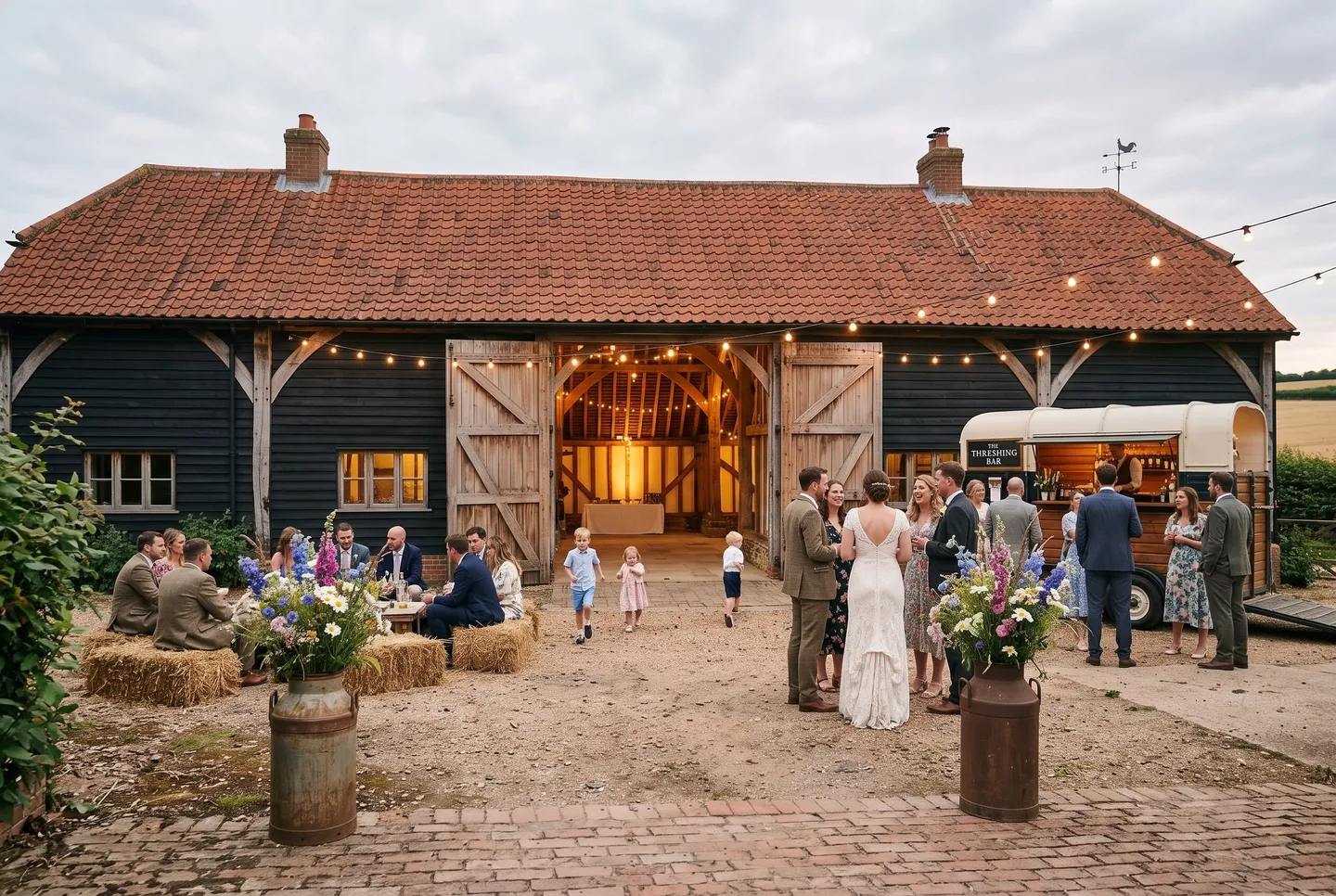 Guests gather with drinks among hay bales in the farmyard at The Wedding Barn