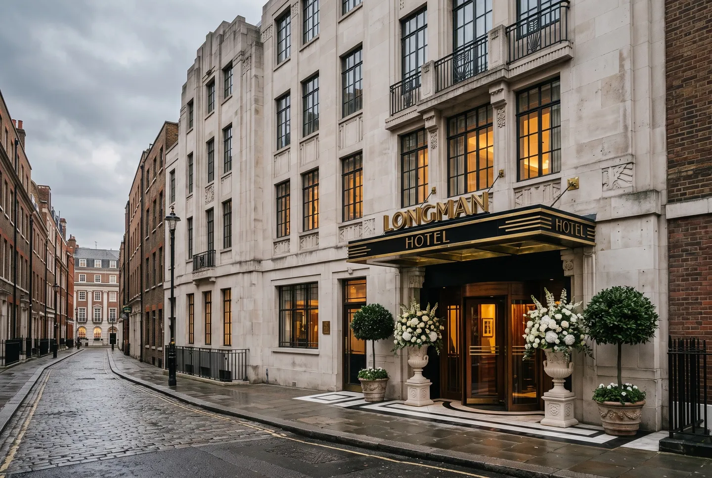 The Portland stone Art Deco façade of Longman Hotel, with bay trees and white flowers either side of the entrance