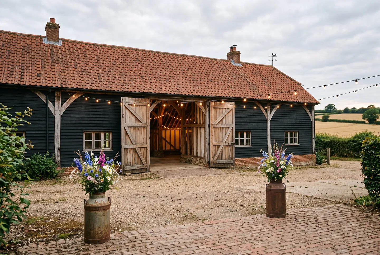 The Wedding Barn, a black weatherboarded barn with its cart doors open onto a farmyard strung with festoon lights