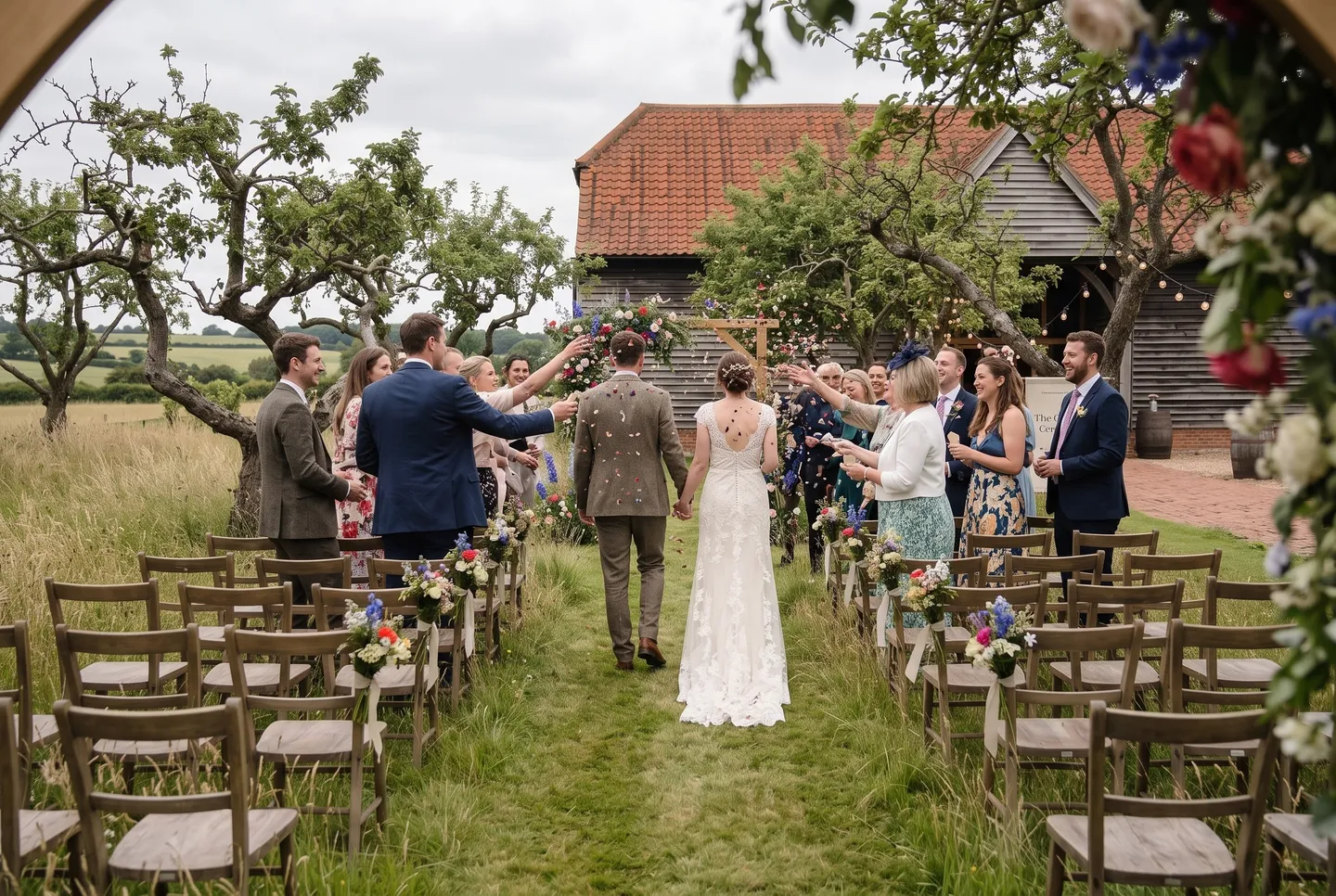Guests throw confetti as a just-married couple walk down the aisle in the Orchard at The Wedding Barn